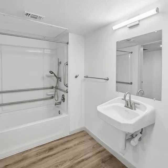 A white sink is mounted on a wall next to a glass shower stall.